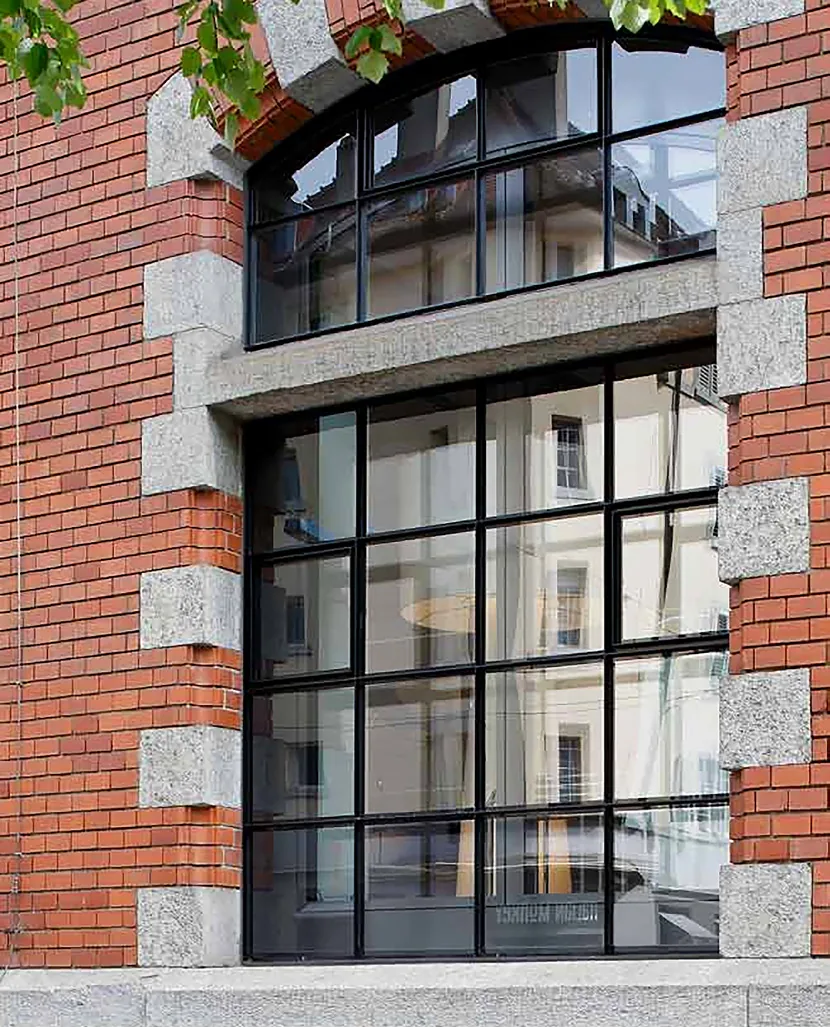 Façade en brique avec grande fenêtre cintrée en acier noir