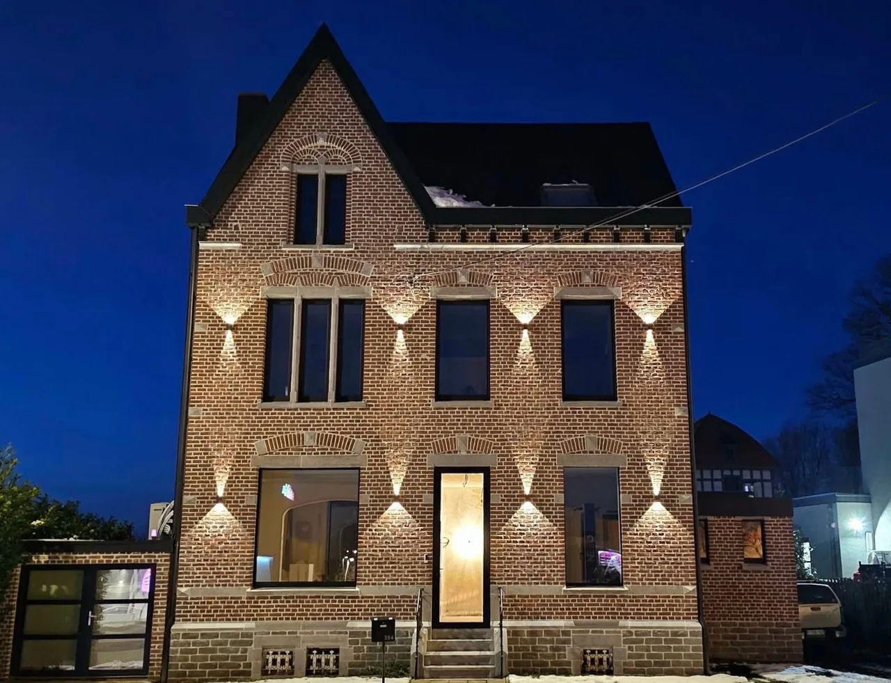 Maison de maître en brique rénovée avec châssis aluminium noirs, éclairée de nuit
