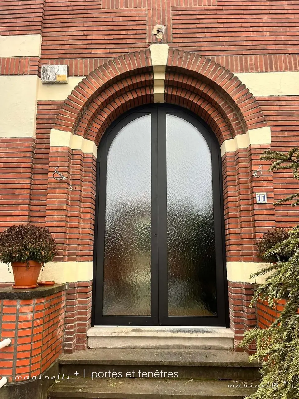 Porte d'entrée cintrée noire à vitrage dépoli dans une façade en brique rouge et jaune
